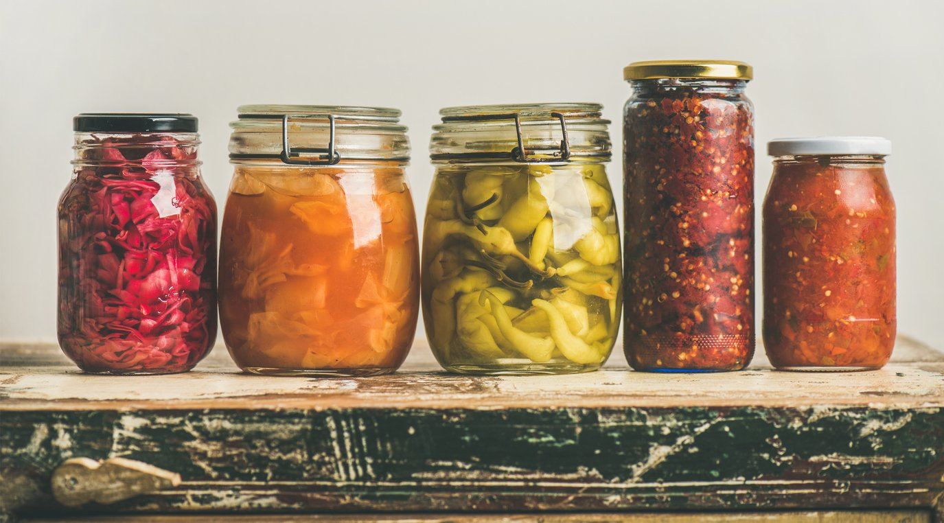 Five different-sized jars of colourful fermented foods lined up on a weathered counter.