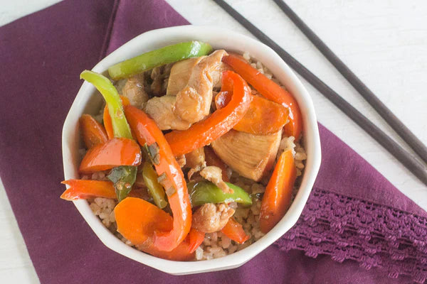 Low FODMAP chicken stir fry with red and green bell peppers and carrots, served over rice in a white bowl with chopsticks on the side
