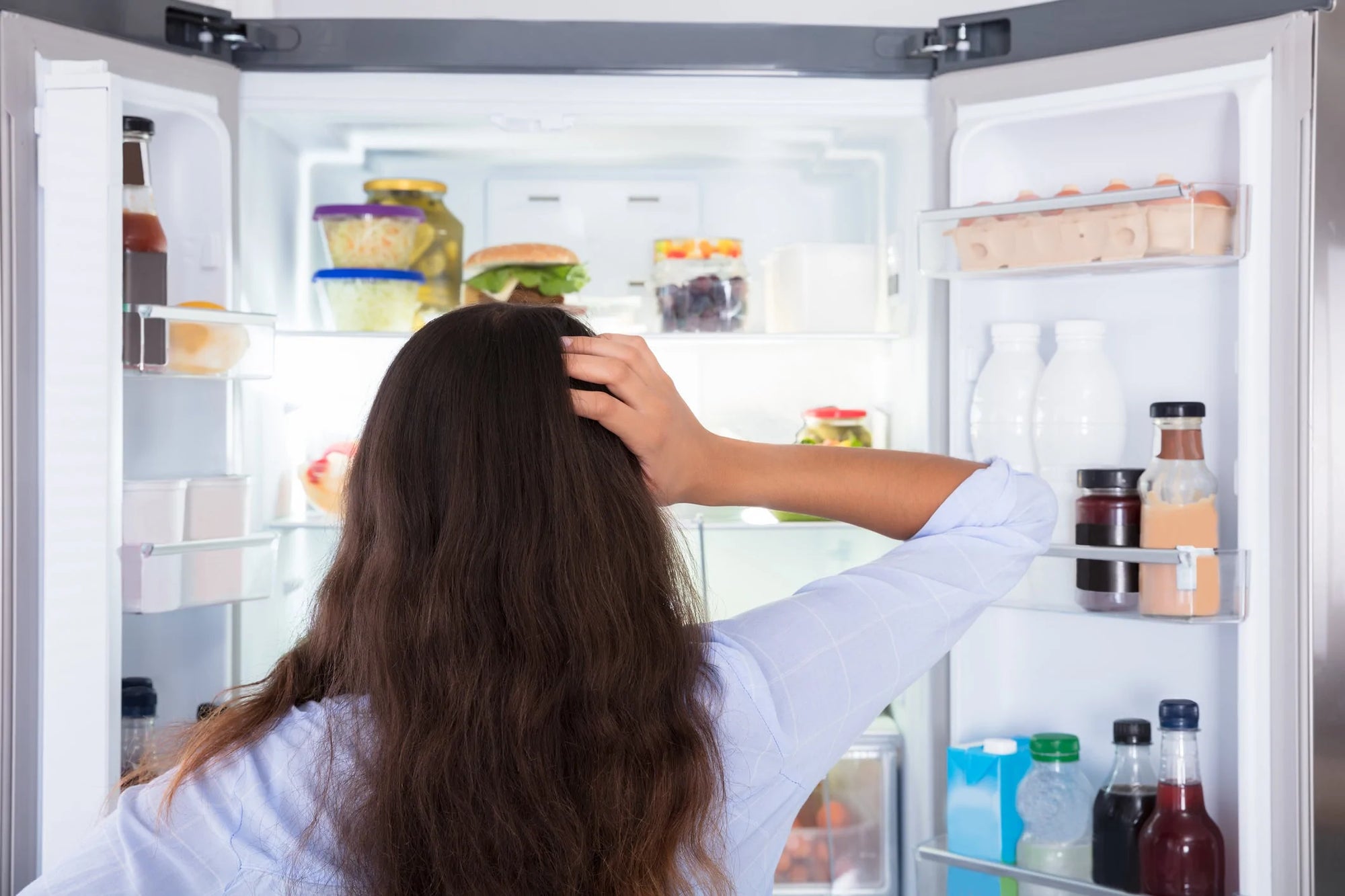 A woman examining the contents of her fridge and wondering how to use leftovers to make a new meal