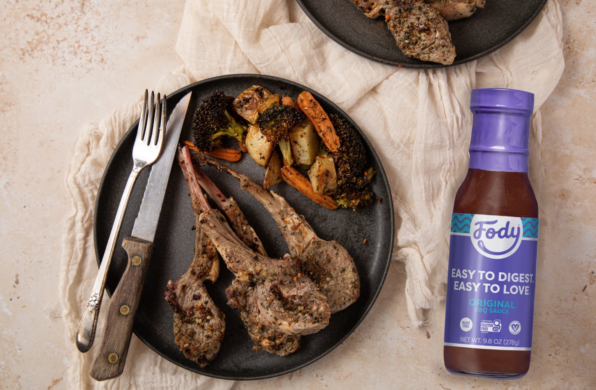 An image of Fody’s Herbed Lamb Chops with BBQ Sauce & Roasted Veggies on a plate beside a bottle of Fody's Maple BBQ sauce.