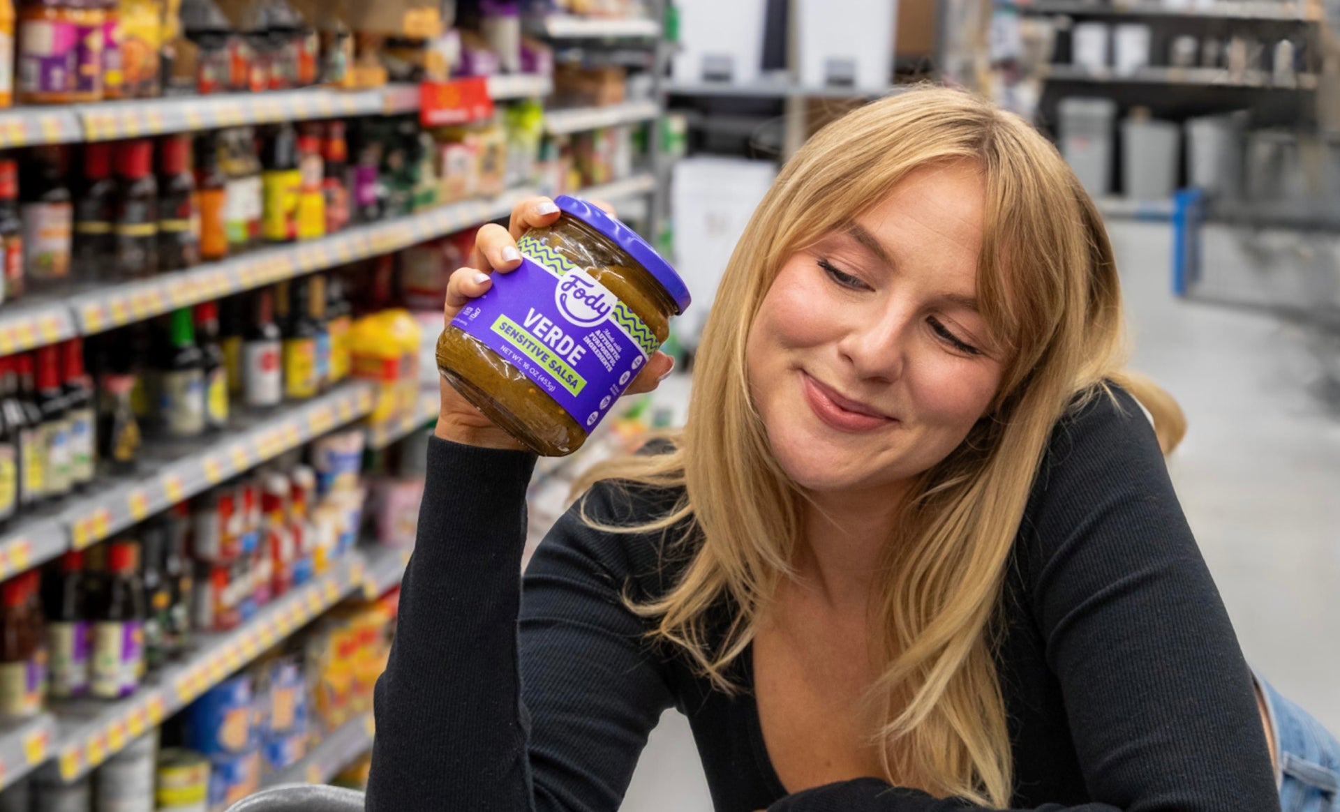 Lady in a supermarket holding a jar of Fody's Verde Sensitive Salsa