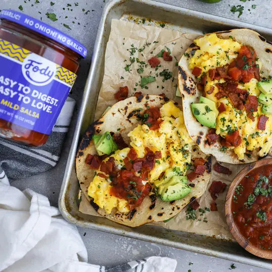 Fody Mild Salsa jar beside breakfast tacos with scrambled eggs, avocado, and salsa on a baking sheet