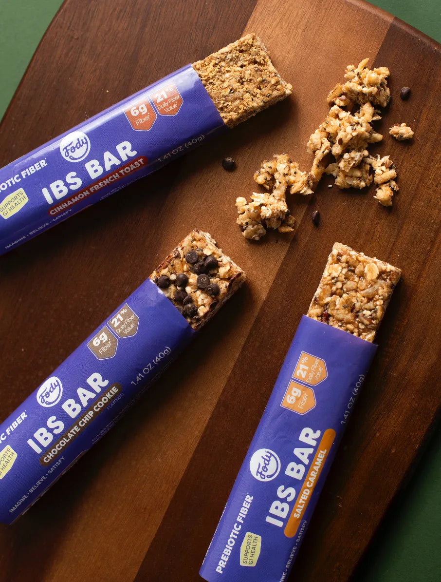 Fody Low FODMAP snack bars in three flavours — cinnamon, chocolate chip, and salted caramel — on a wood cutting board