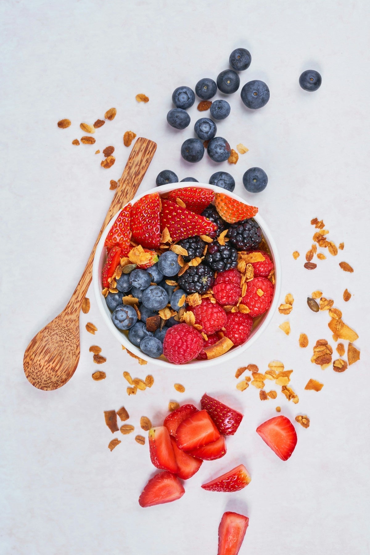 Low FODMAP berry bowl with blueberries, raspberries, strawberries, blackberries, and granola, wooden spoon alongside