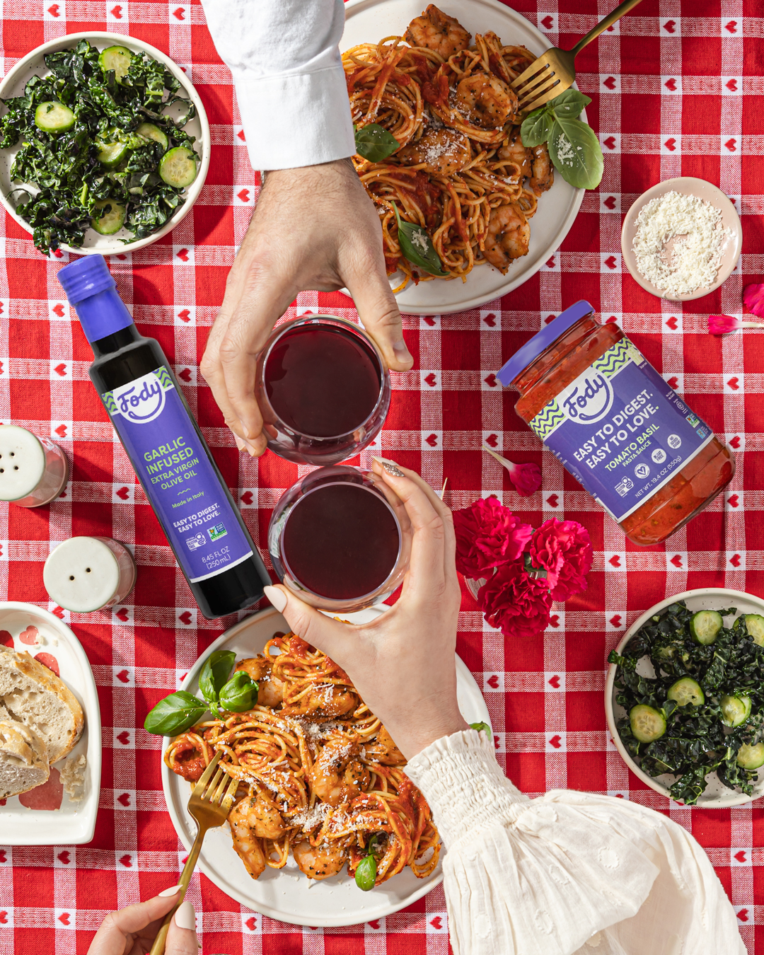 Two hands toasting glasses of wine over a table of gut-friendly Valentine’s Day meals.