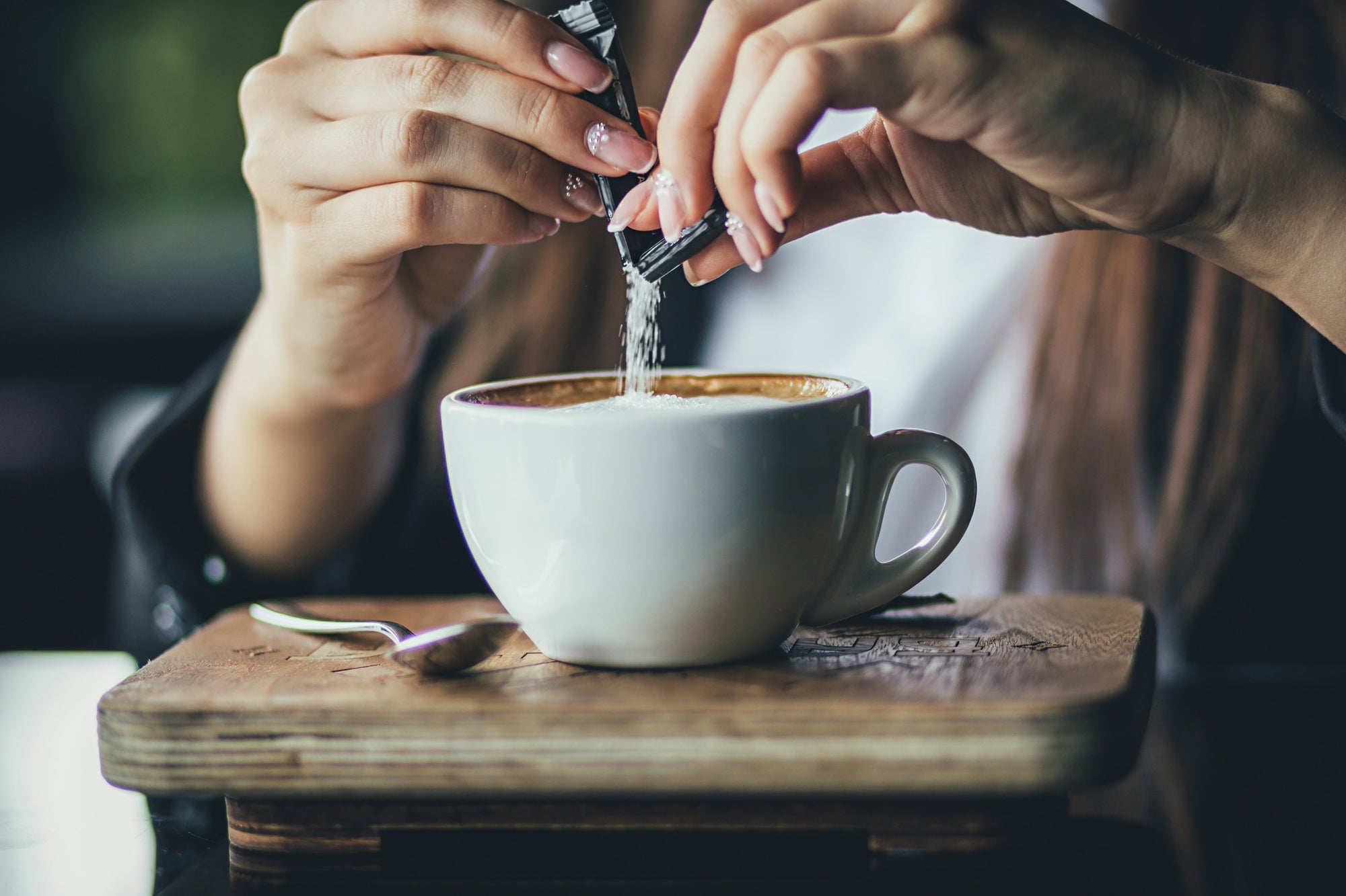 Artificial sweeteners and gut health: a hot topic! Image: a closeup of a woman’s hands pouring a packet of sweetener into a cappuccino.