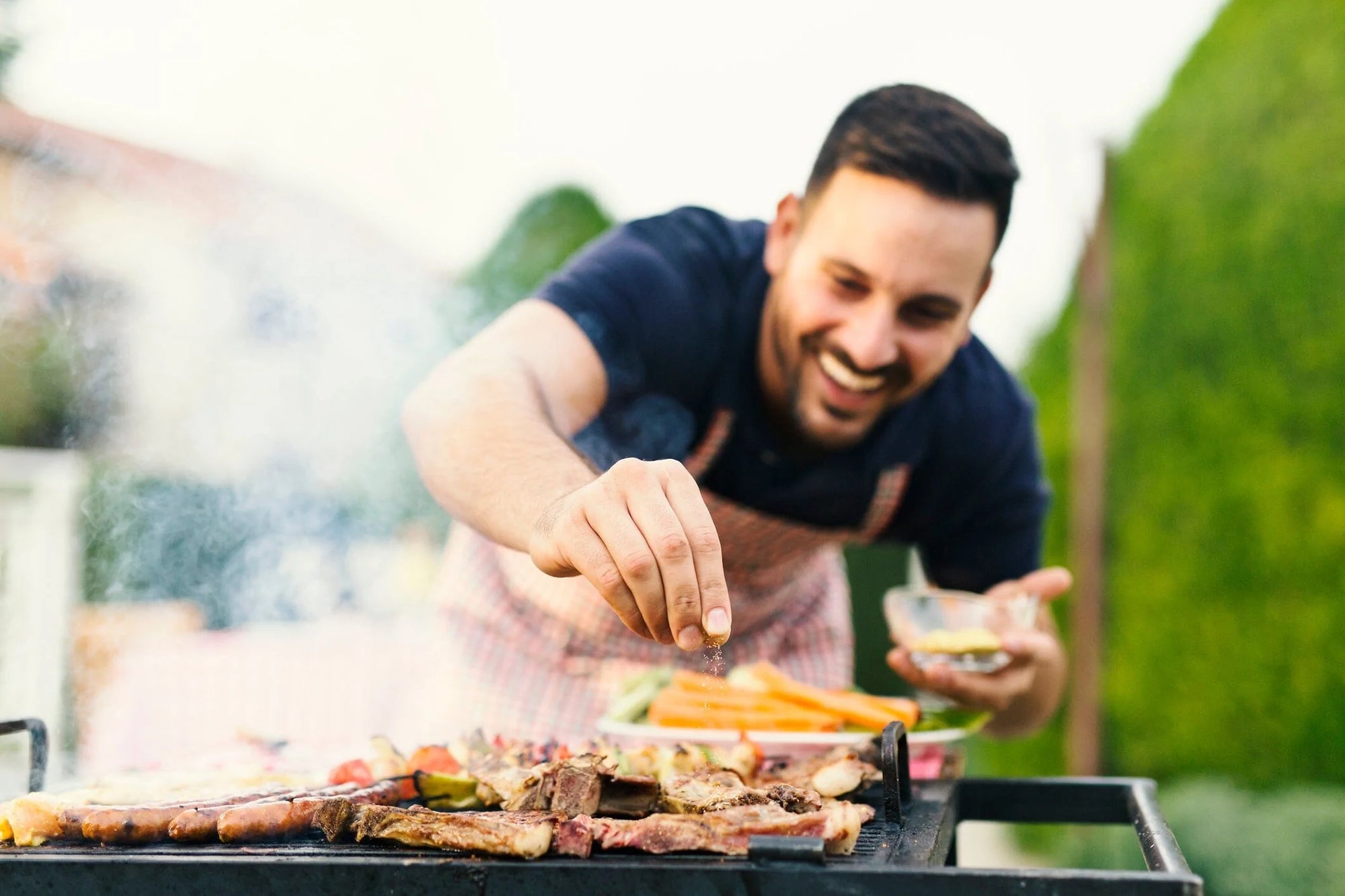A man barbecuing, happily sprinkling an onion substitute or seasoning onto his grilling meat.