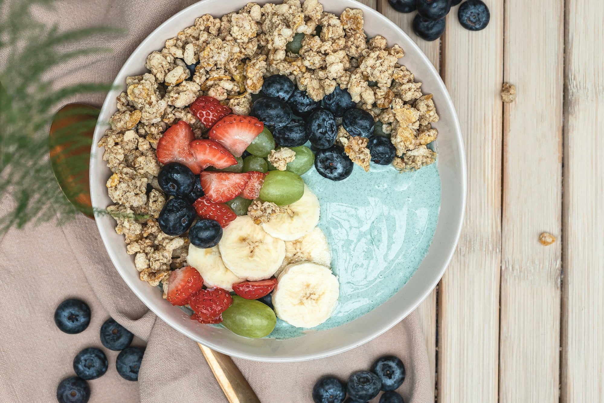 A white bowl of granola and yogurt topped with fresh blueberries and mixed fruit on a wooden table, representing food-based prebiotic fiber sources discussed in a guide to prebiotic supplements for gut health.