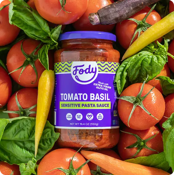 Jar of Fody Tomato Basil Pasta Sauce nestled among fresh tomatoes, rainbow carrots, and greens, a simple base for a Low FODMAP meal